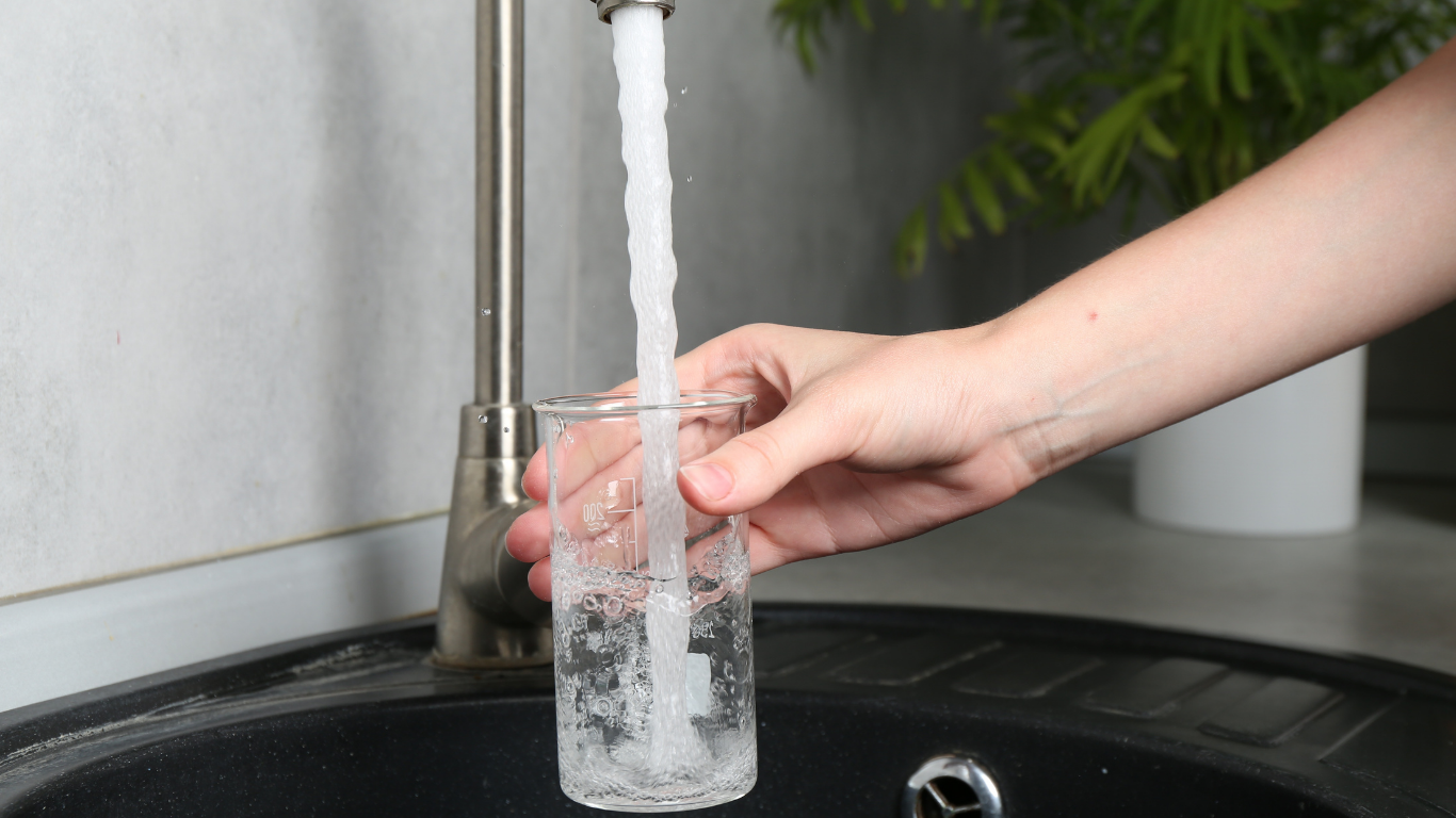 Plumber adjusting waste pipework beneath a double kitchen sink.