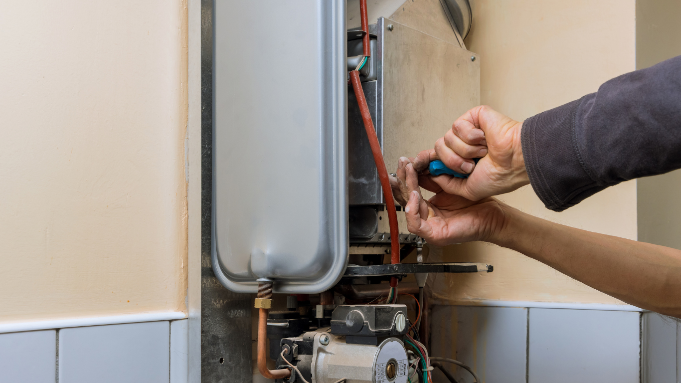 Heating engineer working on copper pipework inside an open boiler Underfloor heating manifold with circulation pump, control valves and connected pipework.