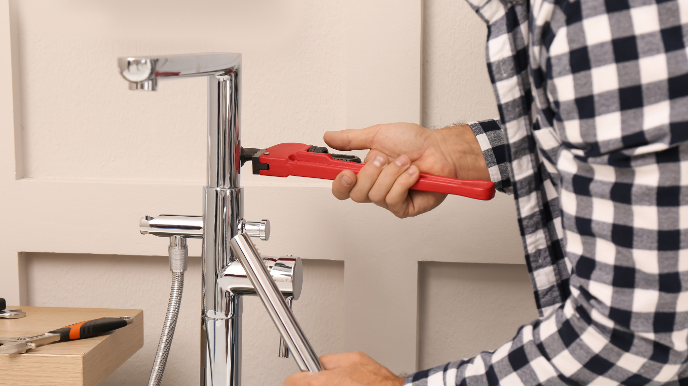 Plumber adjusting waste pipework beneath a double kitchen sink.