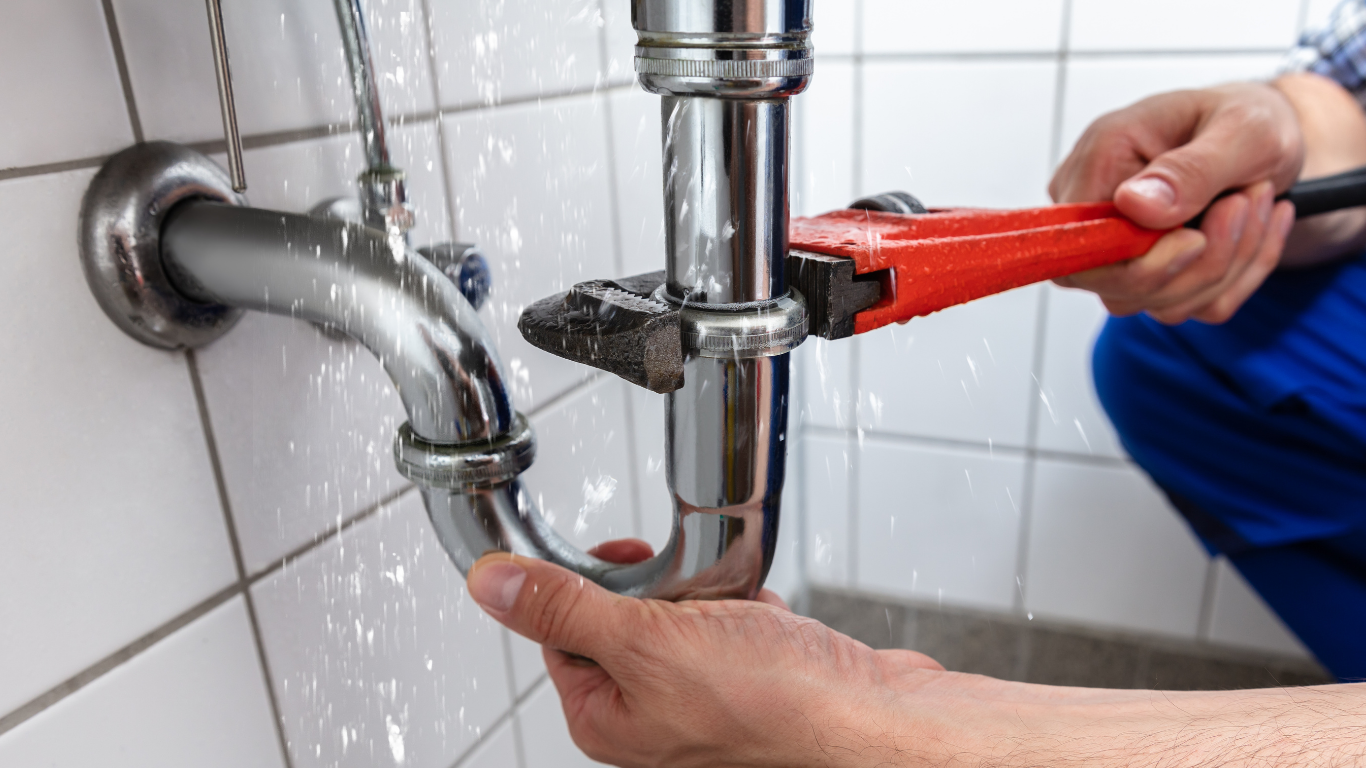 Plumber adjusting waste pipework beneath a double kitchen sink.