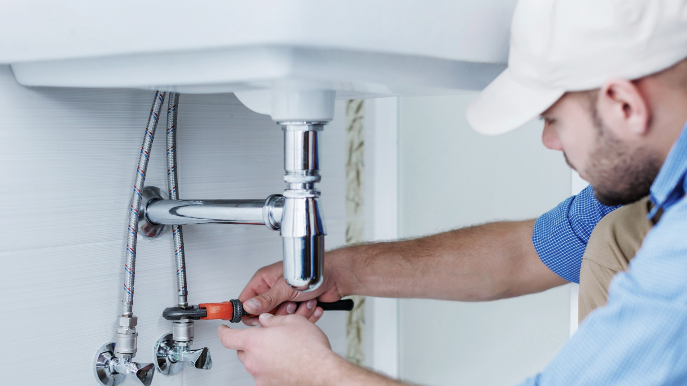 Plumber adjusting waste pipework beneath a double kitchen sink.